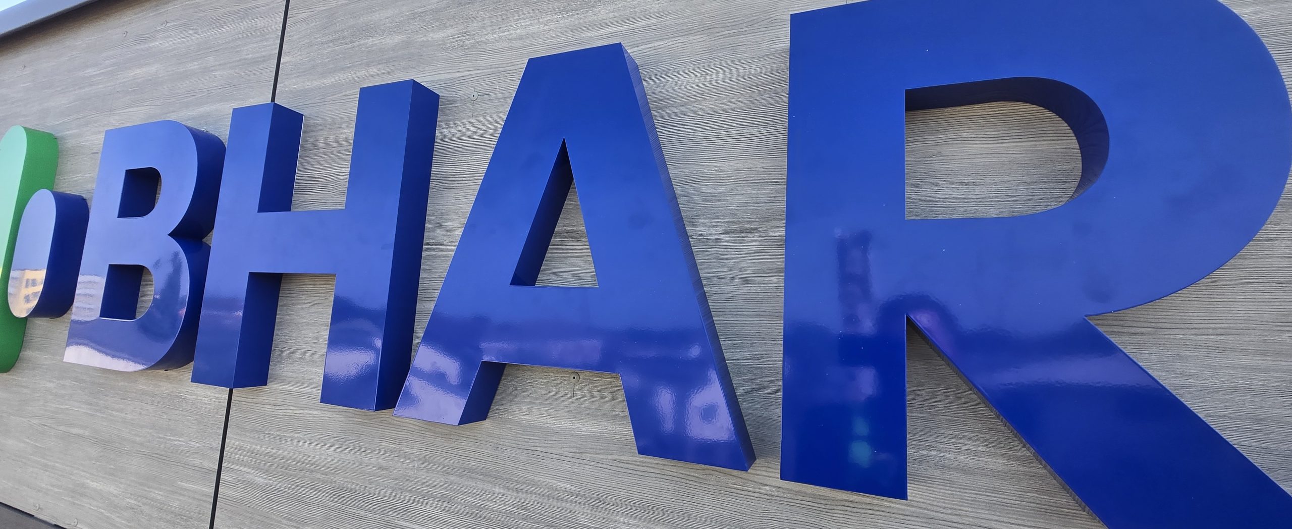 Close-up of blue dimensional letters spelling BHARANI mounted on grey cladding, viewed at an angle