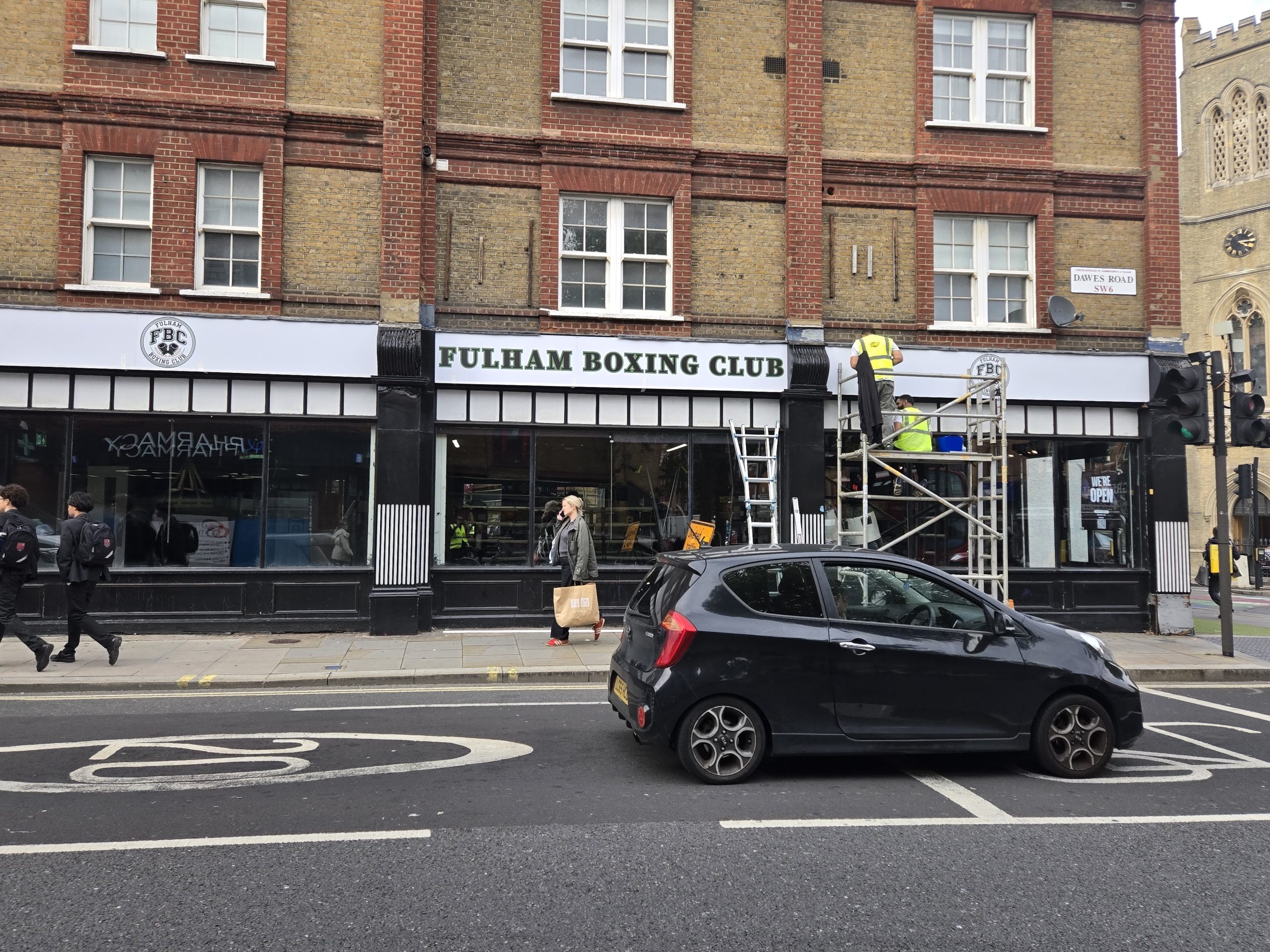 White Fulham Boxing Club fascia panels across the frontage, with installation taking place beside a busy road.