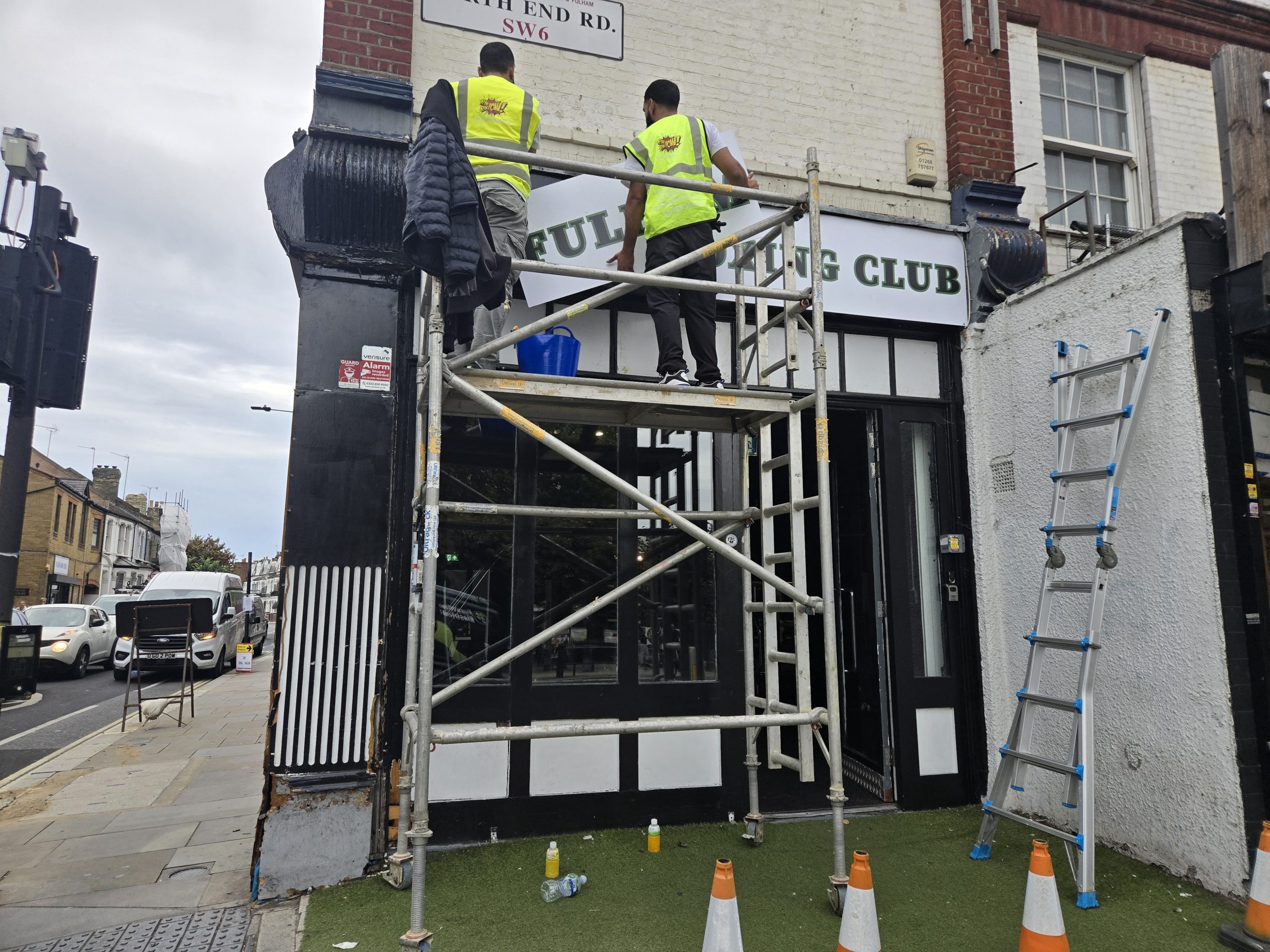 Installation team fitting Fulham Boxing Club’s white fascia panels from a mobile access tower.