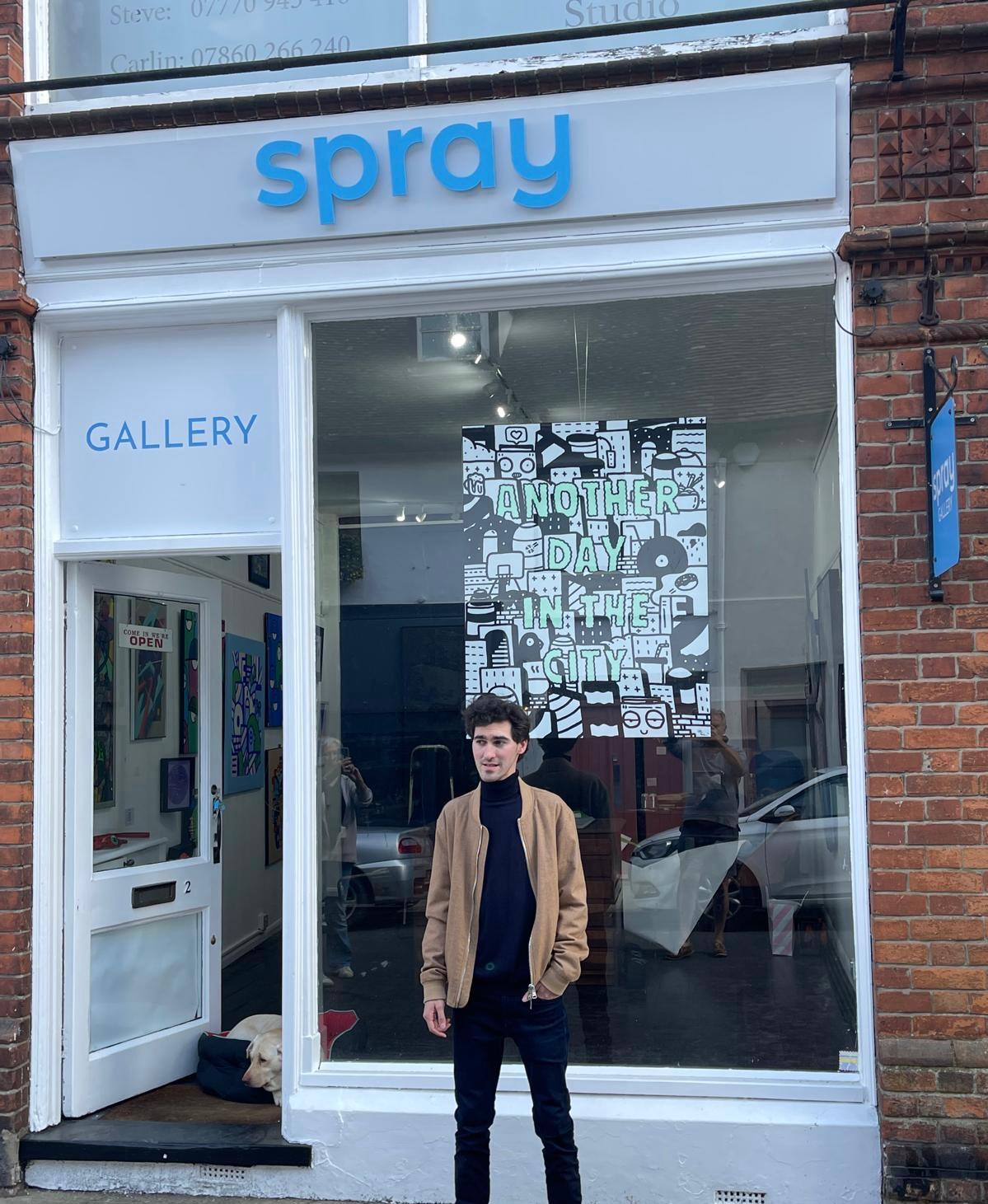 A person standing outside Spray Gallery, with the completed blue fascia lettering and window display behind them.