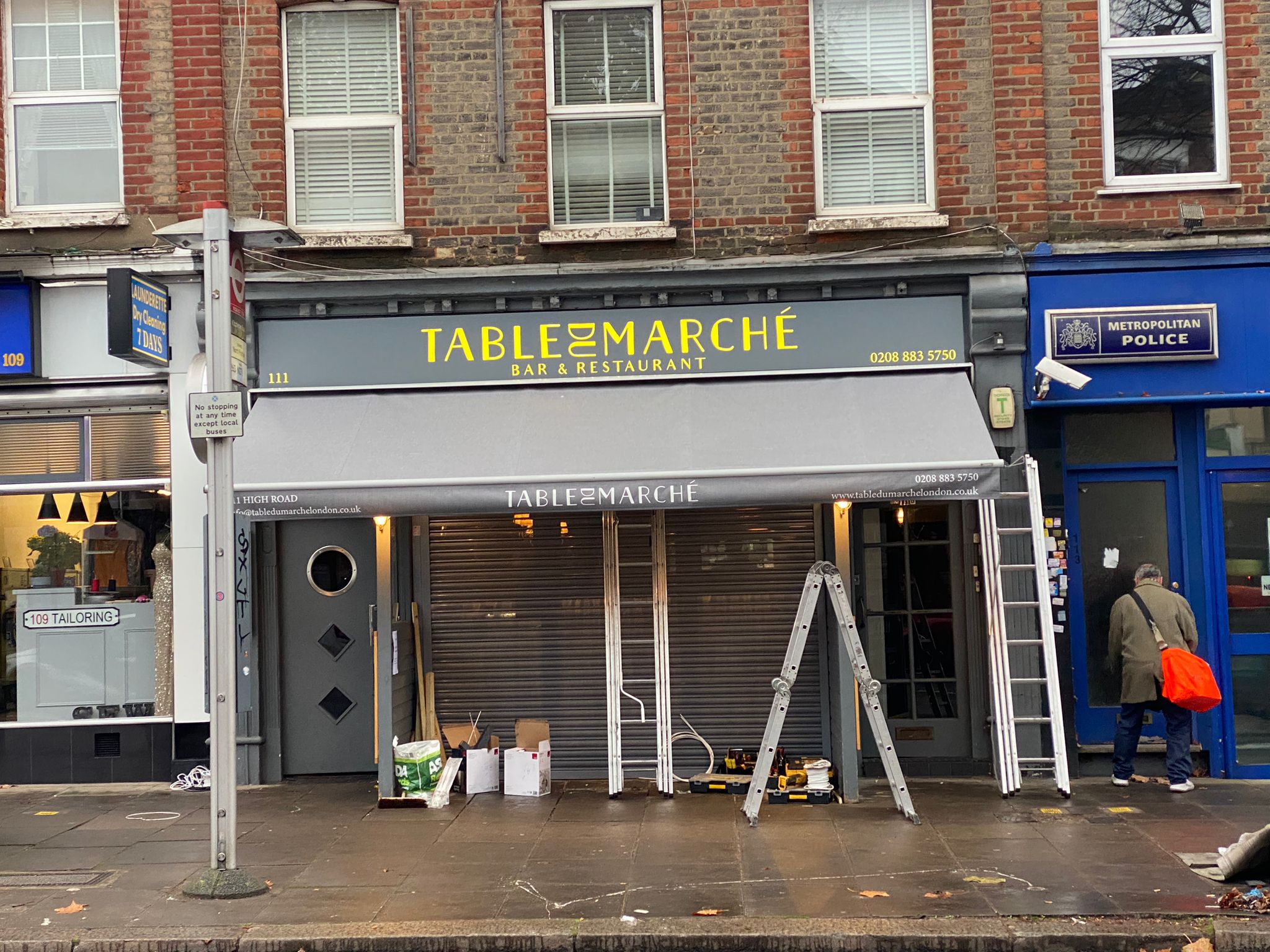 Front view of Table du Marché during installation, showing the fret-cut sign and ladders outside the restaurant.
